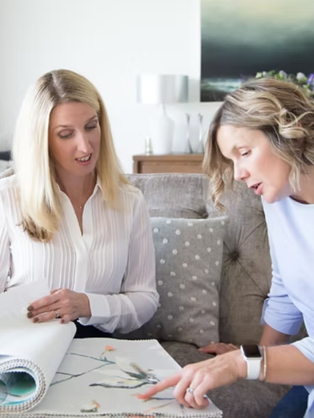 Two women reviewing a fabric sample book together during a home consultation